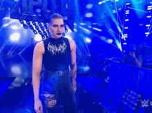a man in a black tank top and black pants is standing on a stage in front of a blue background .