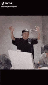 a man in a black hat is standing in front of a computer with his arms in the air .