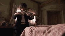 a young boy in a suit plays a violin in a bedroom