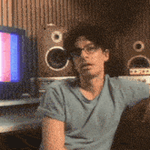 a man wearing glasses and a blue shirt is sitting on a couch in front of speakers .