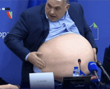 a man with a very large belly is sitting at a table with microphones and a sign that says b. haursi