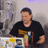 a man wearing a halloween safety t-shirt sits in front of a laptop