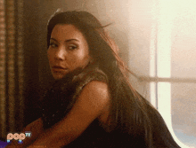 a woman with long hair is sitting in front of a window with a pop tv logo on the bottom