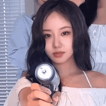 a woman is holding a hair dryer in her hand and looking at the camera .