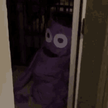 a purple stuffed animal with big eyes is standing in a doorway .