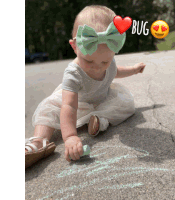 a baby wearing a green bow is playing with chalk on the ground