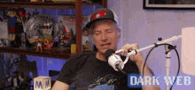 a man wearing a hat is sitting in front of a microphone with the words dark web above him .