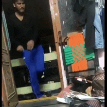 a man in a black shirt and blue pants is dancing in a room with clothes hanging on the wall .