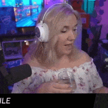 a woman wearing headphones holds a glass of water in front of a microphone