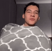a man is wrapped in a gray and white blanket and making a funny face .