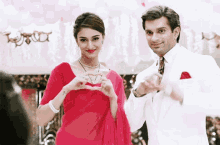 a man and a woman are making a heart shape with their hands .