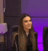 a woman is sitting in a chair in front of a purple wall and smiling .
