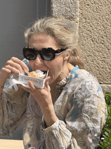 a woman wearing sunglasses and a paisley shirt is eating a pastry from a box that says hotel de palma