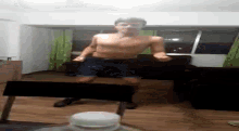 a shirtless man is standing in a living room next to a laptop .