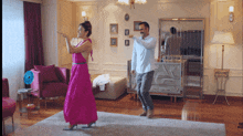 a man and a woman are dancing in a living room and the woman is wearing a pink dress
