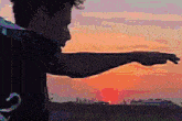 a man is pointing at the sunset while wearing a black jacket that says ' abercrombie & fitch ' on it