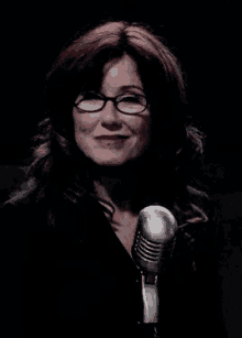 a woman with red hair and glasses is standing in front of a microphone .
