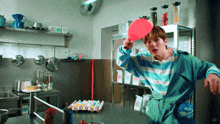 a man in a blue and white striped shirt is holding a red paddle in a kitchen
