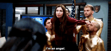 a woman in a red sweater is surrounded by a group of men in gold jumpsuits and says i 'm an angel