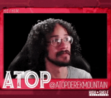 a man with curly hair and glasses is sitting in a chair with the name atop at the top