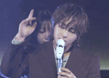 a man in a suit is singing into a microphone while a woman looks on