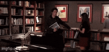 a man and a woman are standing in a library looking at books .
