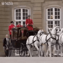 a man in a red uniform is driving a horse drawn carriage with white horses .