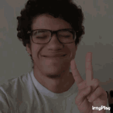 a man wearing glasses and a white shirt is giving the peace sign