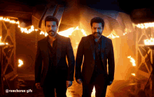 two men in suits are standing in front of a fire and a ramcharan gif