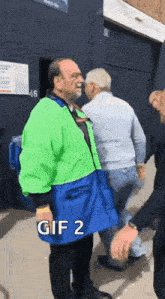 a man in a green and blue jacket is standing next to another man in a blue skirt .