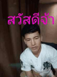 a young man in a white shirt is sitting on a couch with a pink background that says สวัสดี