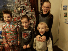 four children are posing in front of a christmas tree with one wearing a shirt that says superman