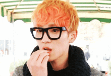 a young man with orange hair and glasses eating something