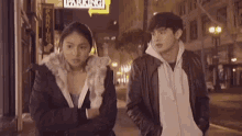 a man and a woman are standing in front of a parking sign