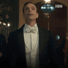 a man in a tuxedo and bow tie looks up at the hbo logo in the background