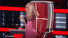 a woman in a pink dress is sitting in a chair with nbc written on the bottom