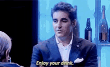 a man in a suit is talking to another man and says enjoy your drink