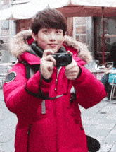 a young boy in a red jacket is taking a picture with a camera .