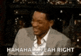 a man in a suit is laughing and saying `` yeah right '' while sitting at a table .