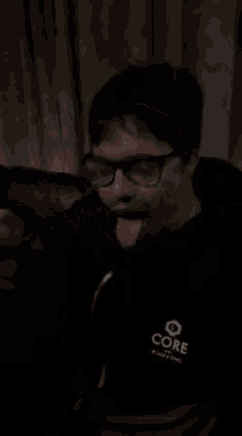 a man wearing glasses and a black shirt that says core is sitting on a couch