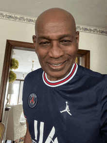 a bald man wearing a paris saint-germain jersey smiles for the camera