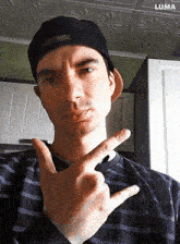 a man wearing a baseball cap and a striped shirt is making a peace sign