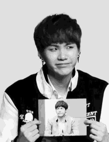 a young man is holding a picture of himself and the word ent is on the jacket he is wearing