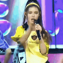 a woman singing into a microphone wearing a yellow shirt that says new york on it