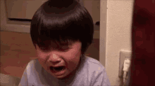 a little boy is crying in a room with his eyes closed .