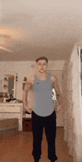 a man in a blue tank top and black pants stands in a hallway