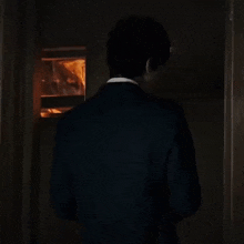 a man in a suit and tie is standing in a dark room looking out of a window .