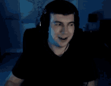 a man wearing headphones is smiling and waving his hand in a dark room