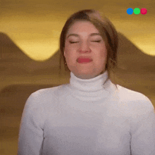 a woman in a white turtleneck is making a face with her eyes closed