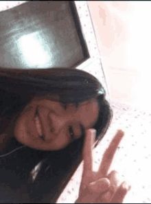 a young girl is taking a selfie and giving a peace sign .
